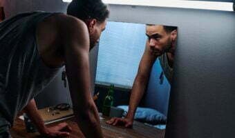 Young man with post traumatic disorder bending over table and looking in mirror